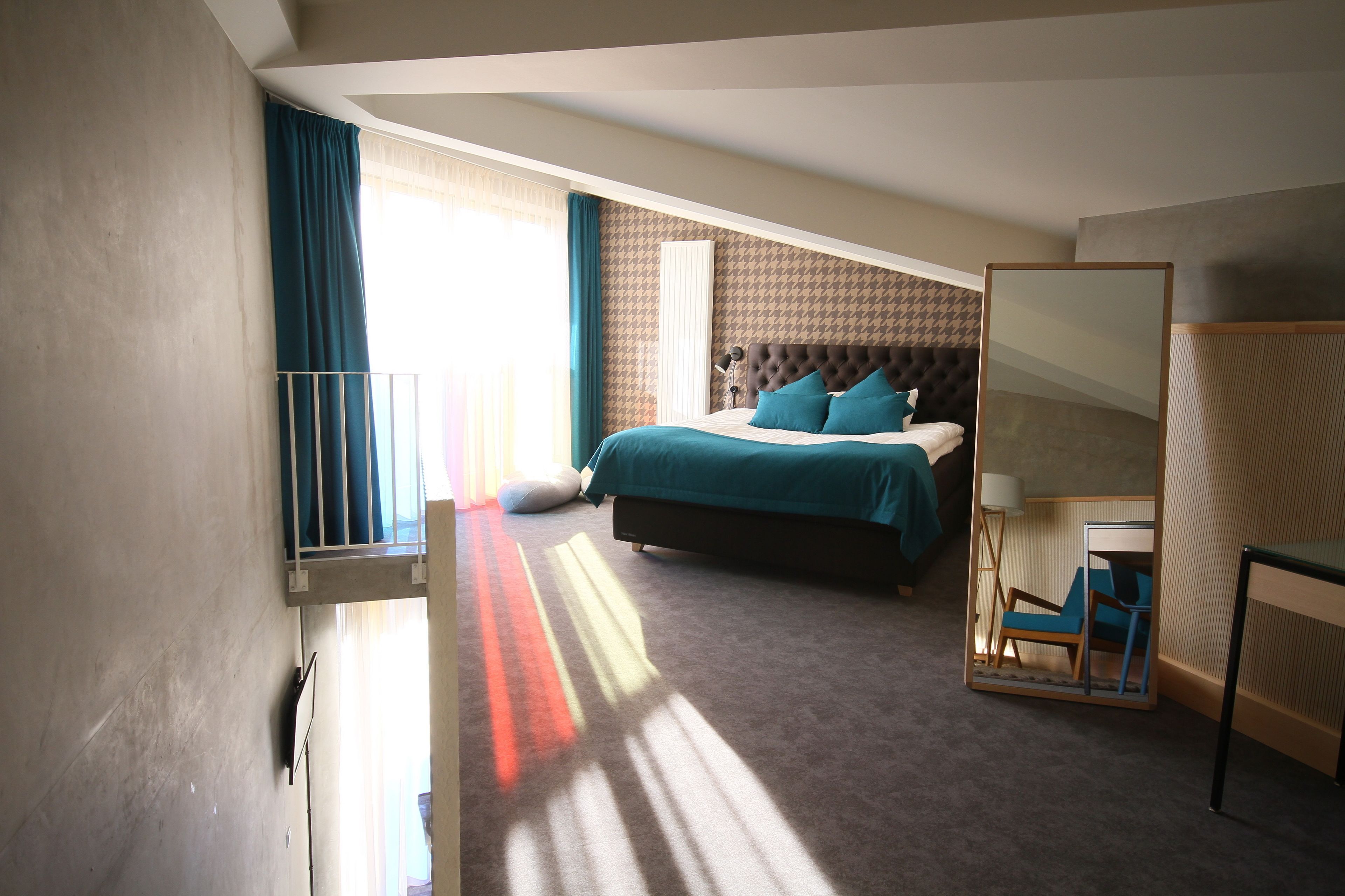 A bedroom with a bed, a desk, and a chair. There is a window with curtains and a view of the outside.