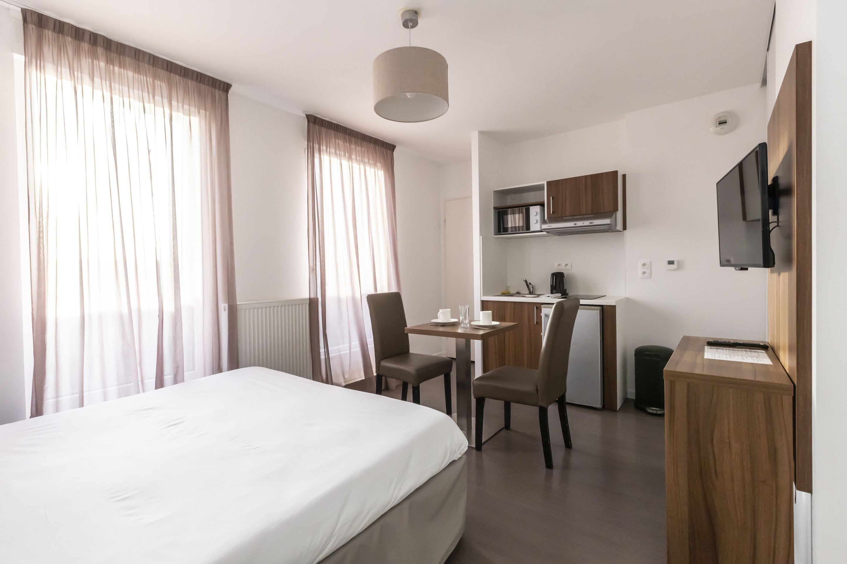 Una habitación de hotel con cama, escritorio, silla, televisor y kitchenette.