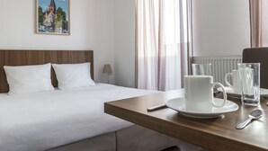 A hotel room with a bed, a wooden headboard, a table with a white mug and glass, and a poster of a church on the wall. - Odalys City Campus Apartment Hotel - Metz Centre (Metz)