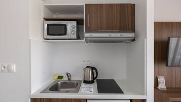 A compact kitchenette with a microwave, stove, sink, and a kettle.