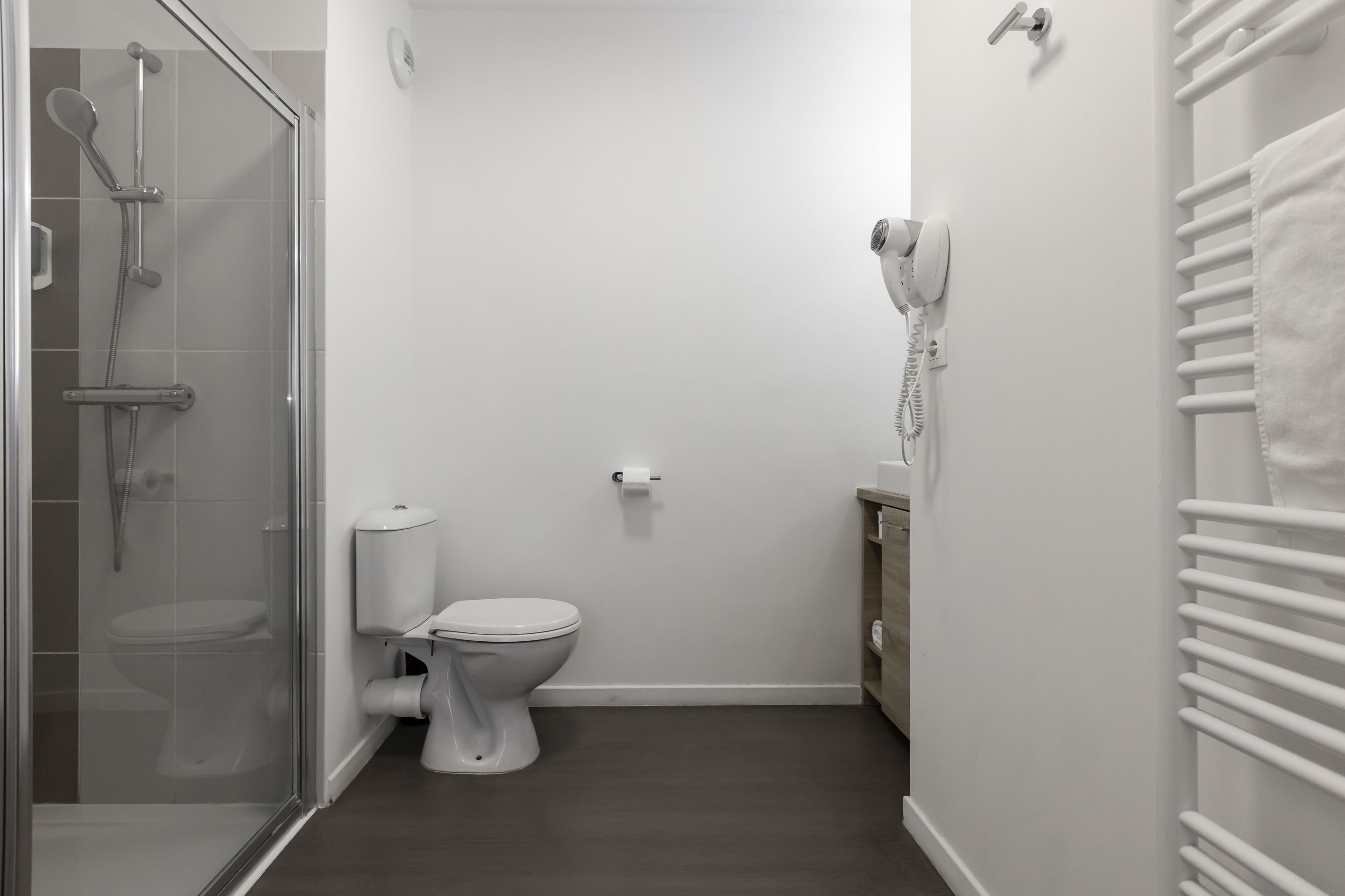 Ein Badezimmer mit einer Duschkabine, einer Toilette und einem weißen Handtuchwärmer.