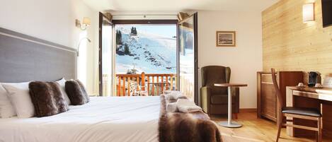 A bedroom with a large bed, a wooden desk, a chair, and a view of a snowy mountain.