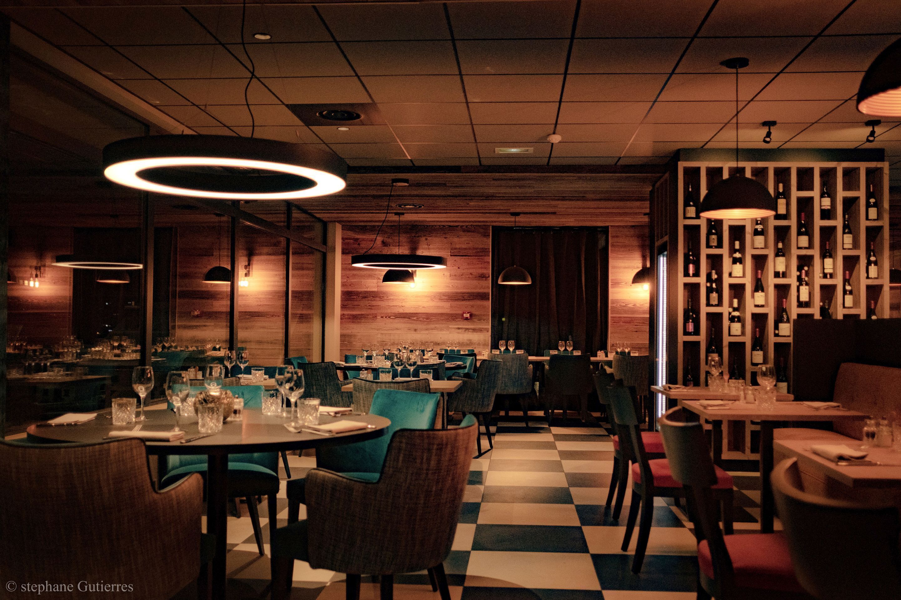 A restaurant with checkered flooring, round tables, and blue chairs.