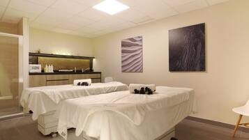 Une salle de spa comprenant deux tables de massage, un comptoir d’accueil et une œuvre d’art accrochée au mur.