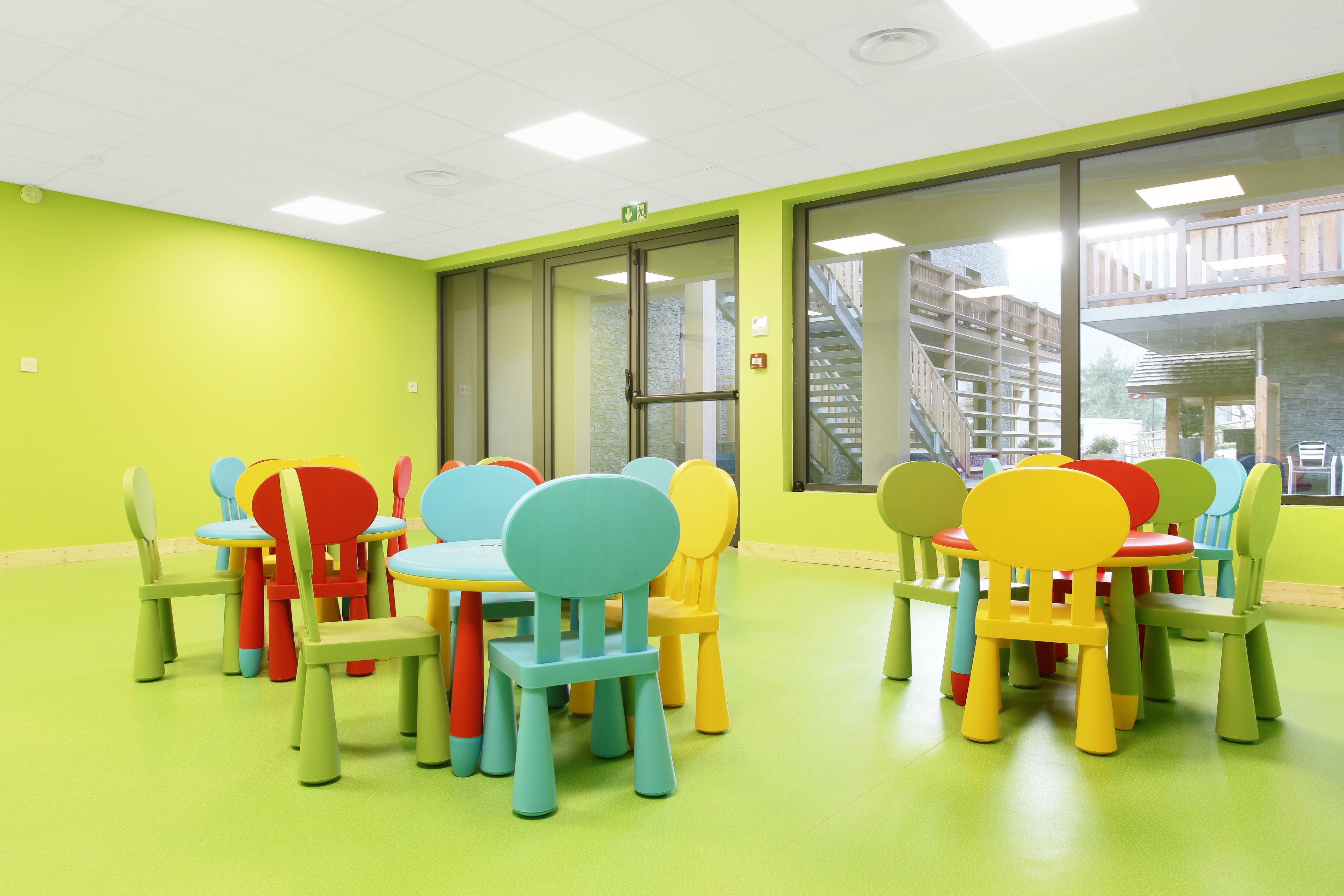 A brightly colored room with green walls and yellow flooring, featuring multiple tables and chairs in various colors.
