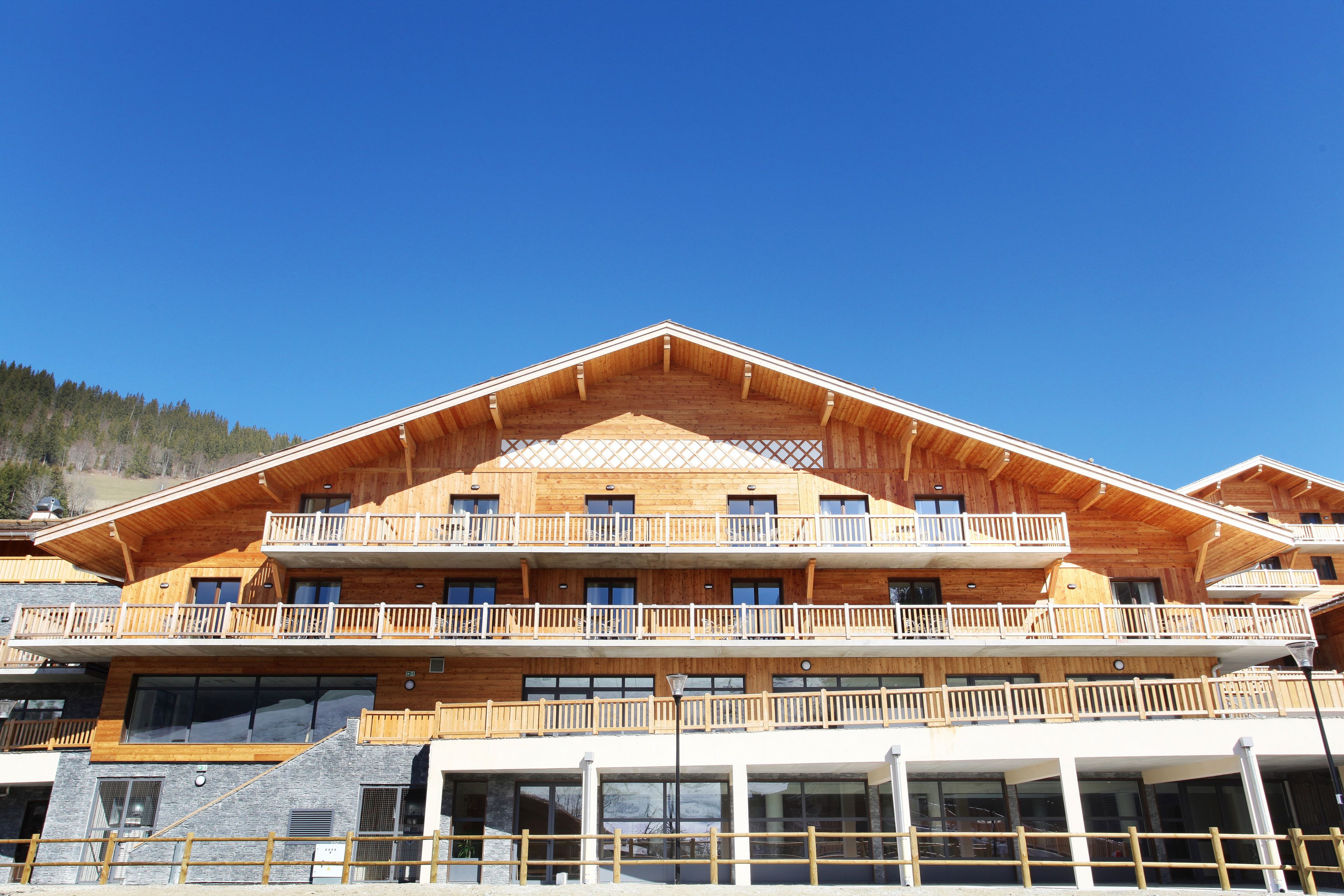 A multi-story wooden building with balconies, large windows, and a clear sky.