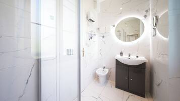 Un baño moderno con piso de mármol, un espejo redondo, un lavamanos y un bidé.