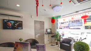 A reception area with a television, a desk with a menu, a door, and a view of the street outside. - GM Hotel Sunway Metro (Petaling Jaya)