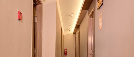 A hotel hallway with carpeted floors, doors on both sides, and fire safety equipment.