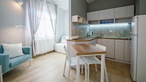 Una cocina moderna con armarios blancos, una mesa de comedor de madera y un sofá blanco en un luminoso salón con un amplio ventanal y cortinas.