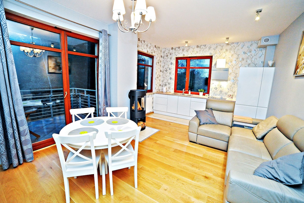 Ein modernes Wohnzimmer mit einer Couch, einem Esstisch mit Stühlen und einer Küchenzeile inklusive Herd und Schränken.