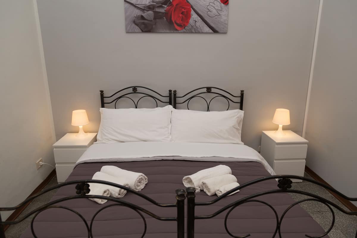 Un lit bien fait, avec du linge de lit blanc, deux lampes de chevet et un tableau encadré au-dessus du lit.