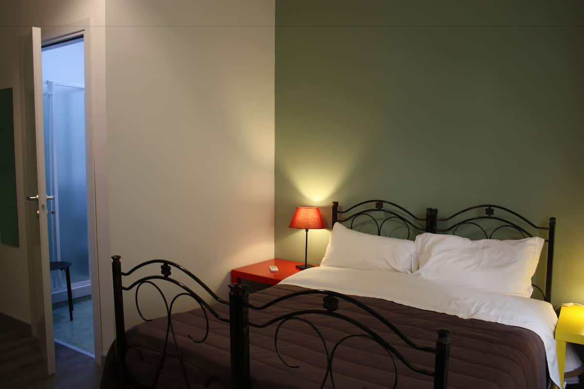 Une chambre à coucher comprenant un lit, une table de chevet, une lampe et une porte donnant sur une autre pièce.