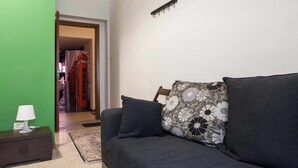 A room with a dark grey sofa, a patterned pillow, a small table with a lamp, and a green wall. - B&B Tra L'Etna e il Mare (Catania)