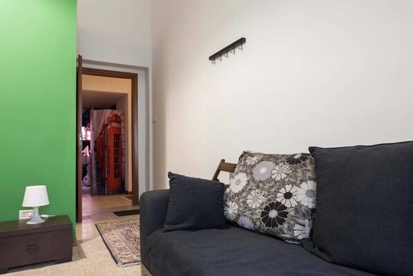 Una habitación con un sofá gris oscuro, un cojín estampado, una mesita con una lámpara y una pared verde.