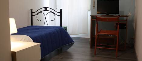 Un dormitorio con cama, escritorio, silla, televisor y lámpara.