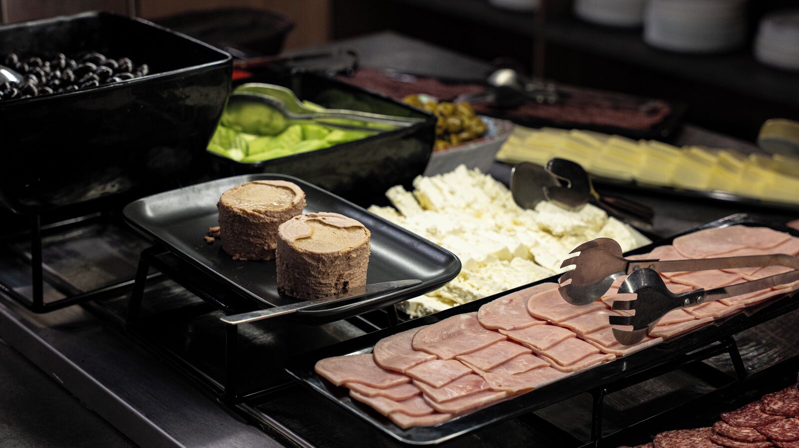 Un bufé con diferentes alimentos, incluyendo carne, queso y un recipiente negro posiblemente para salsas.