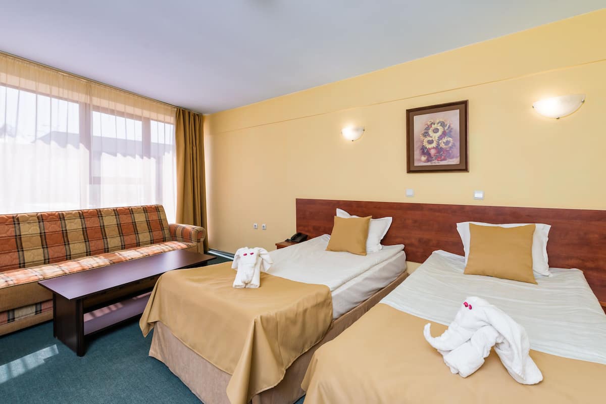 Ein Hotelzimmer mit zwei Betten, einem Sofa, einem Schreibtisch und einem Fenster mit Vorhängen.