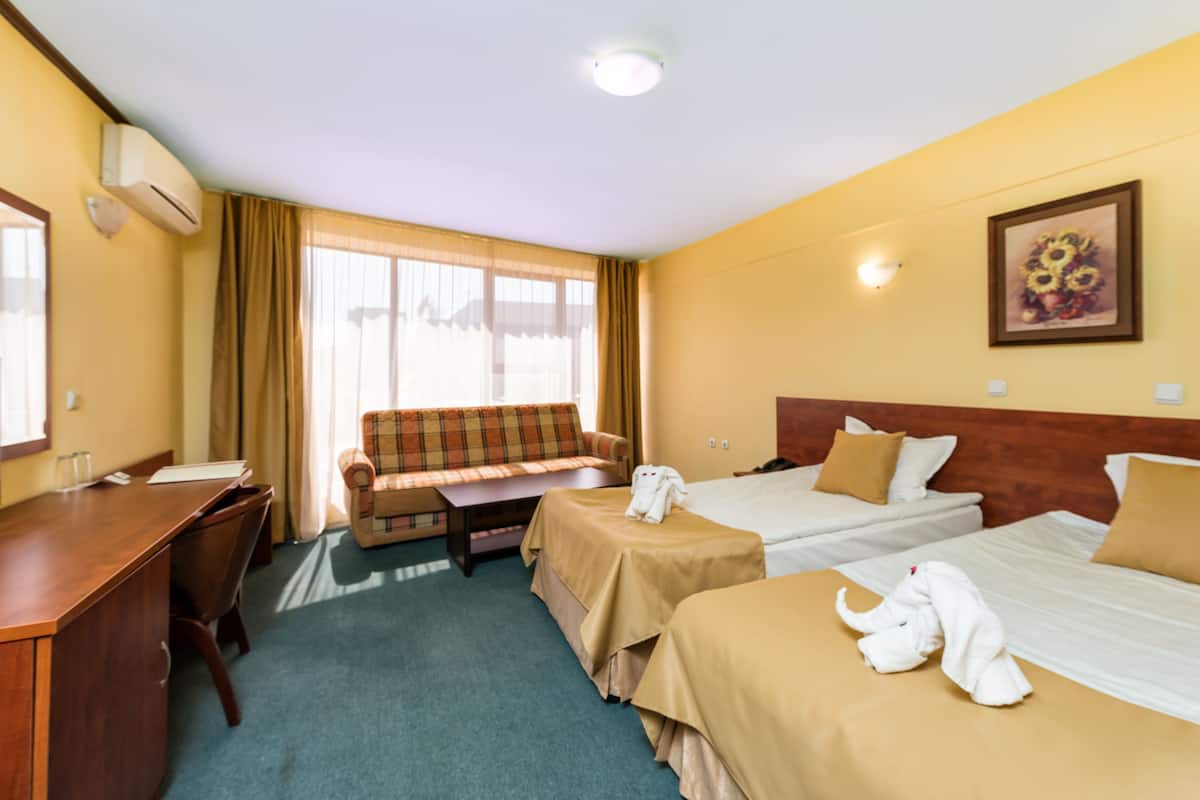 Ein Hotelzimmer mit zwei Betten, einem Schreibtisch, einem Sofa und einem Fenster mit Vorhängen.