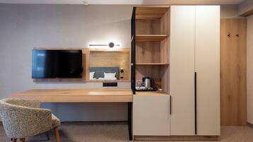 A modern, compact room with a wooden desk, a flat-screen TV, a built-in shelf, and a wardrobe.