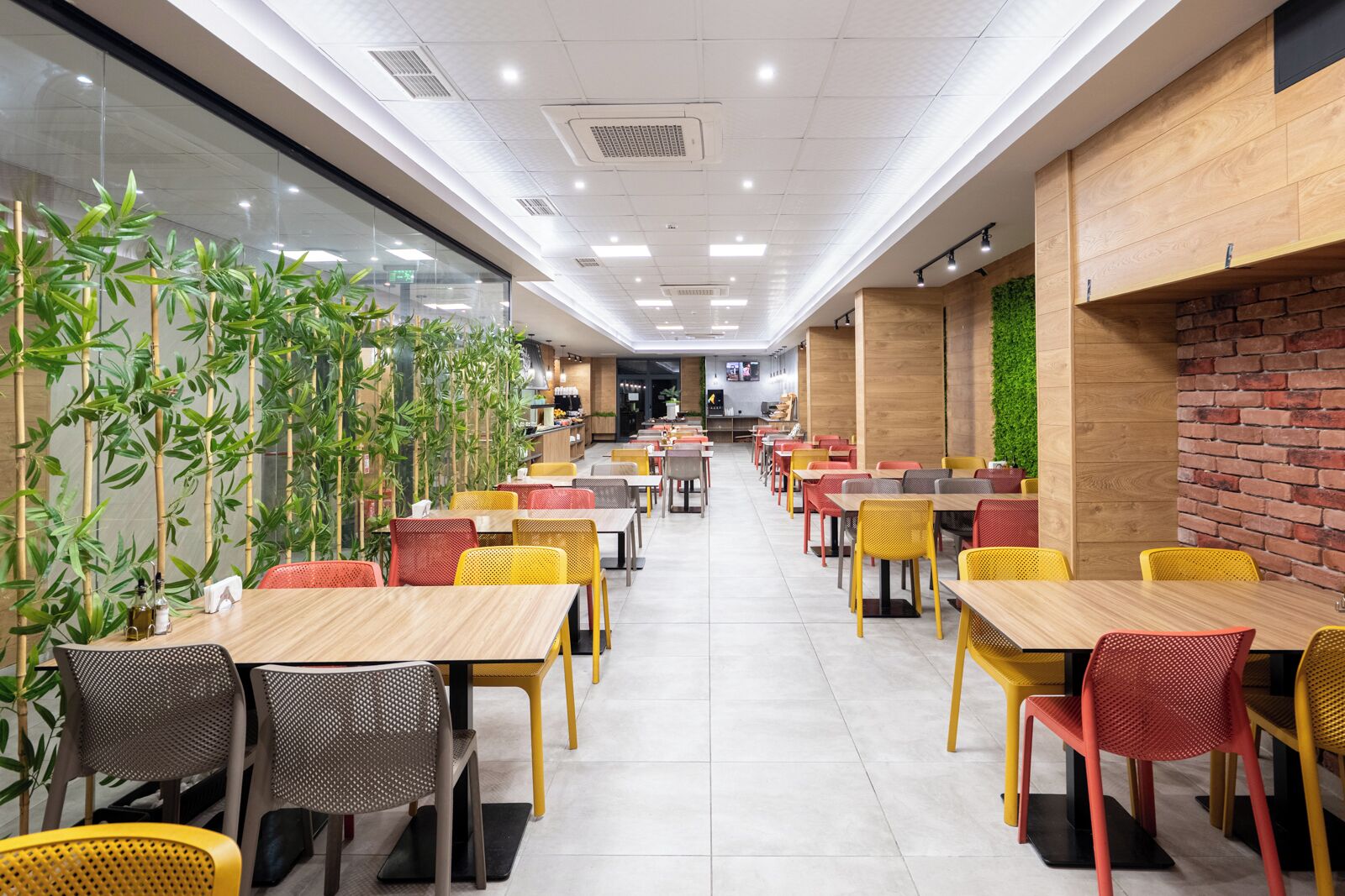 Un amplio comedor interior con varias mesas y sillas, una barra y una pared verde con plantas.