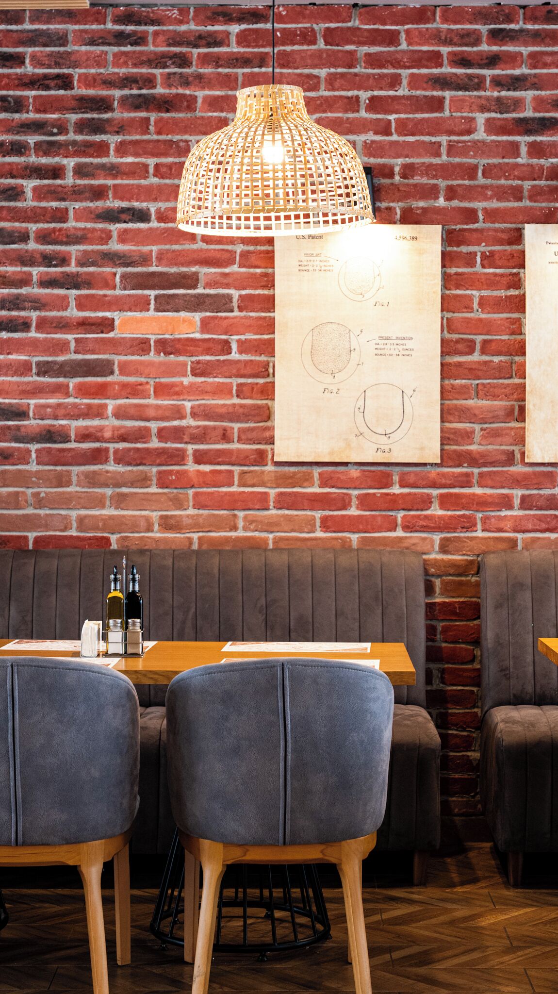 Interior de restaurante con pared de ladrillo, lámpara colgante, mesa de madera y sillas tapizadas en gris.