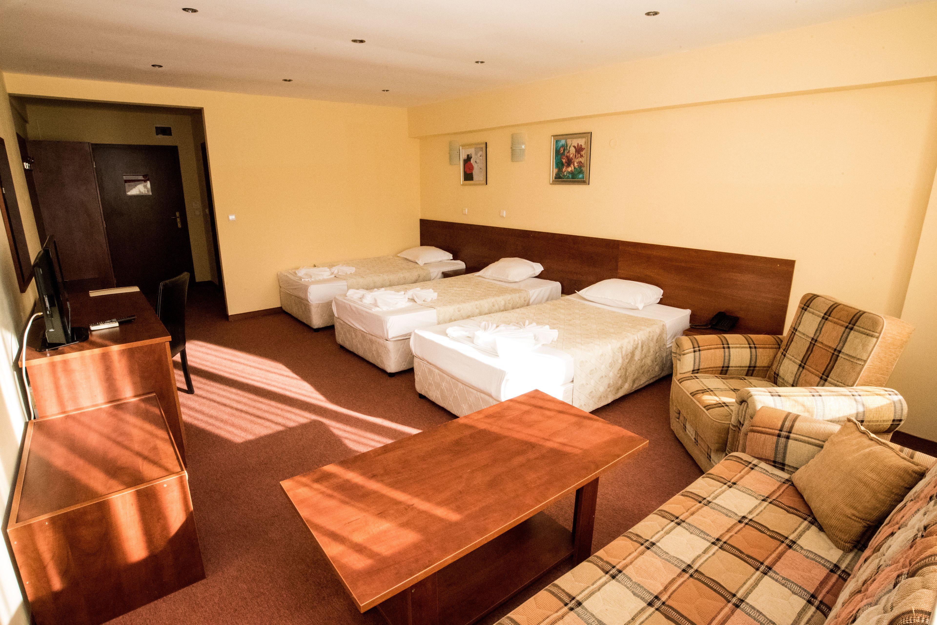 Habitación de hotel con tres camas individuales, un sofá, una mesita de centro de madera y un escritorio con una silla.