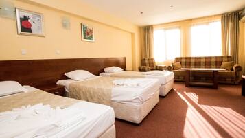 A hotel room with three beds, a sofa, a table, and two wall-mounted lamps.