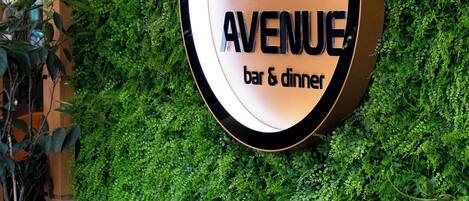 A restaurant sign with a logo and name, surrounded by a green wall and a table with chairs.