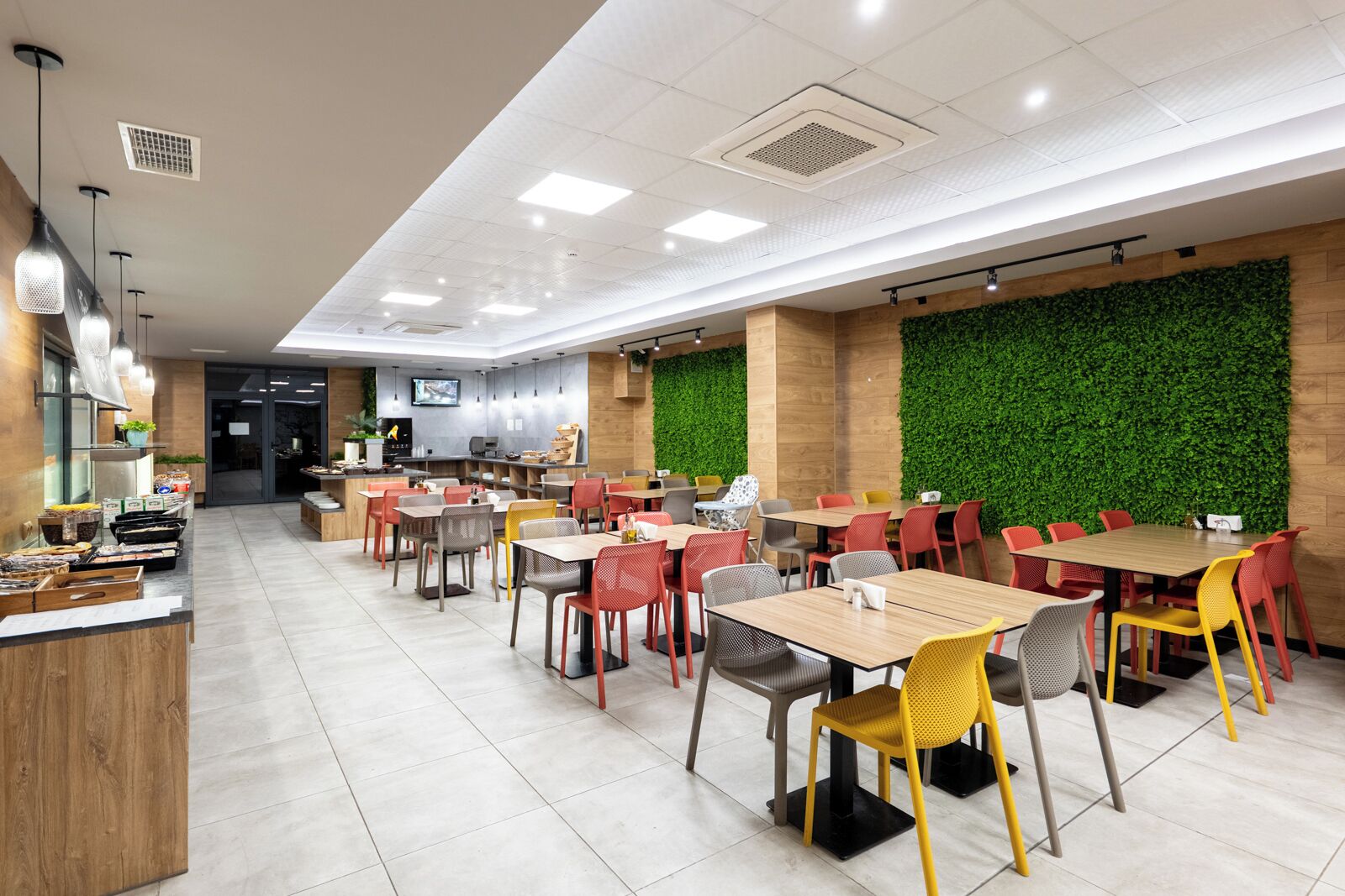 Un restaurante moderno con varias mesas y sillas, una zona de cocina y una pared verde.