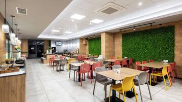Un restaurante moderno con varias mesas y sillas, una zona de cocina y una pared verde.