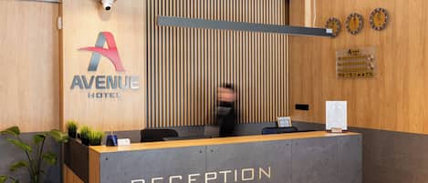 A reception desk with a sign reading "RECEPTION" and a logo for "AVENUE HOTEL".