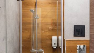 A modern shower with a glass enclosure, wooden wall paneling, and a visible hand dryer.