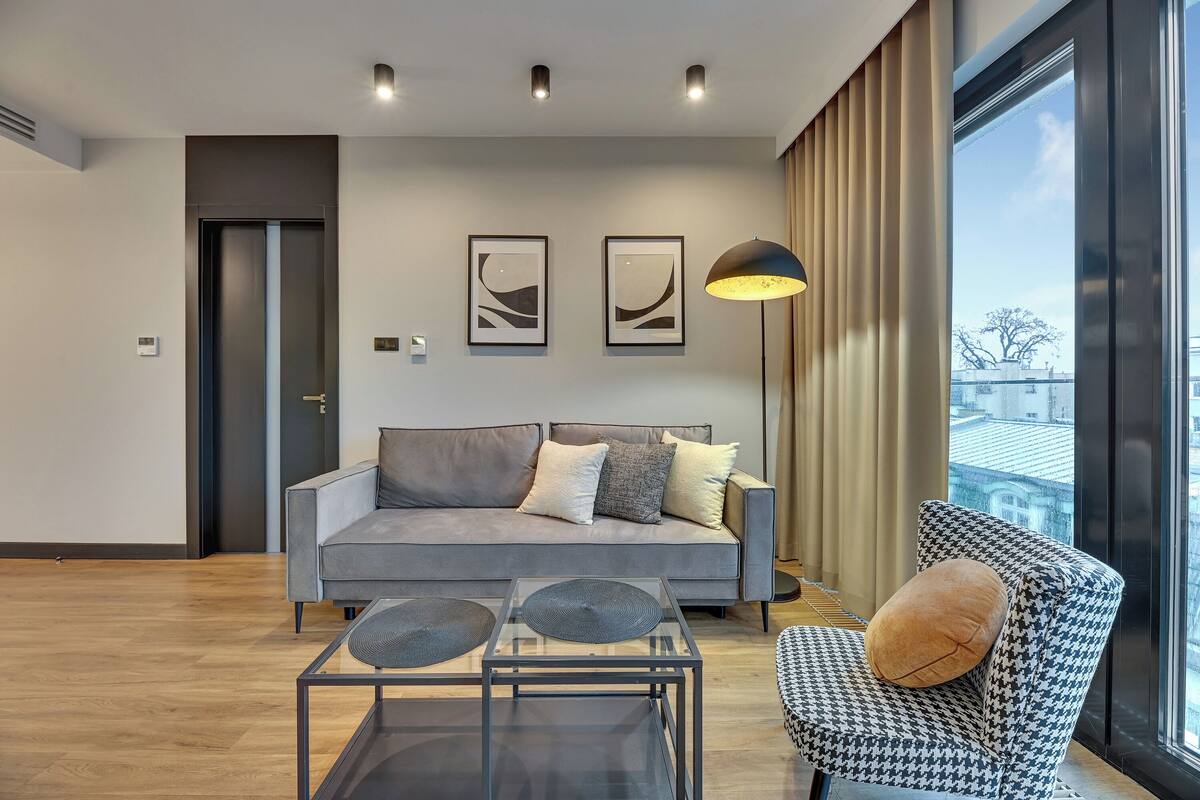 A modern living room with a grey sofa, a patterned armchair, a glass coffee table, and two abstract wall art pieces.