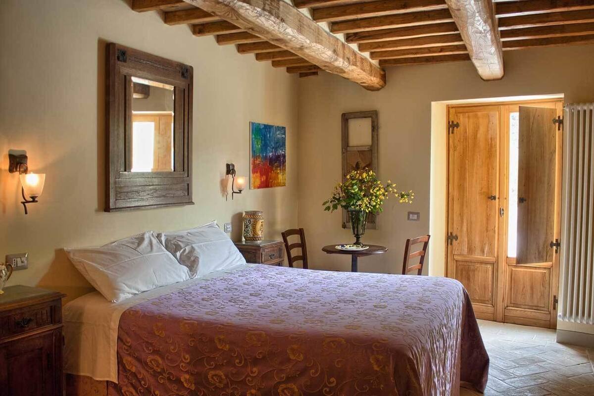 A bedroom with a bed, bedside table, lamp, and a wooden door.