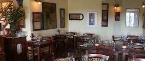 Un comedor con varias mesas y sillas de madera, cada conjunto con platos, cubiertos y vasos.