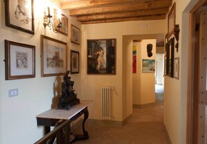 Un pasillo con obras de arte enmarcadas en las paredes, un radiador y una mesa de madera con una escultura.