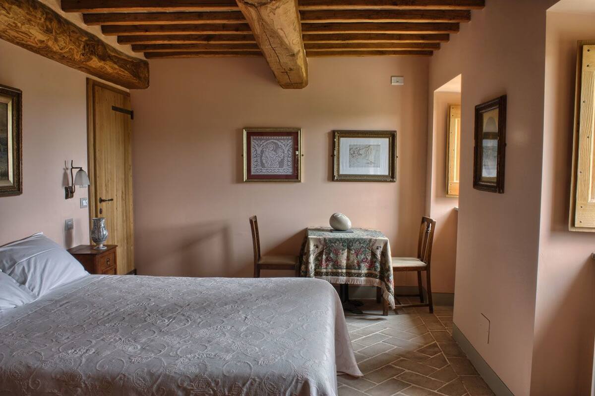 A bedroom with a bed, a small table with a chair, and two framed pictures on the wall.