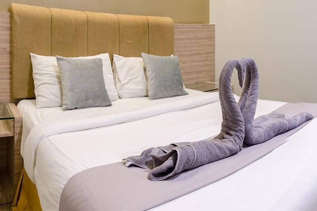 Ein ordentlich bezogenes Bett mit Kopfteil, Kissen und einem in Schwanform drapierten Handtuch.