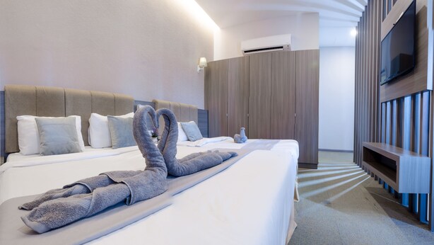 Een moderne hotelkamer met een groot bed, een flatscreen televisie aan de muur en een garderobe met verticale latten.