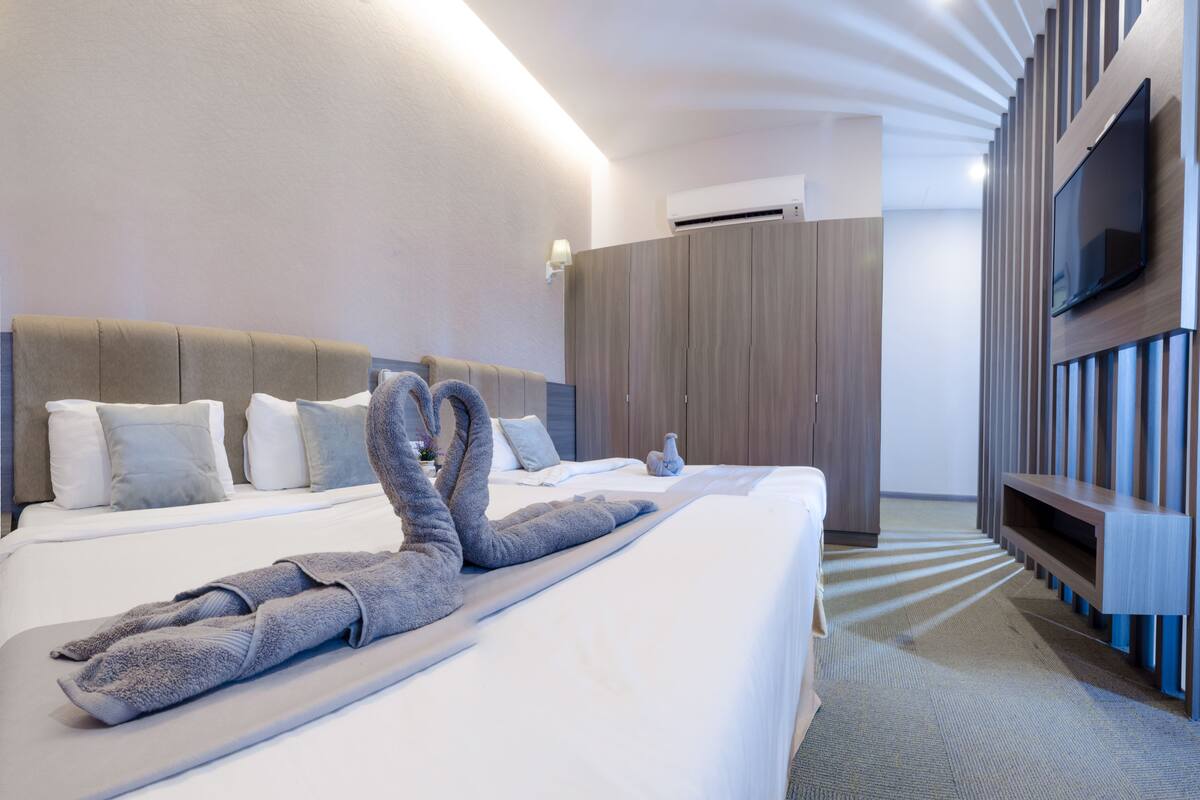 Ein modernes Hotelzimmer mit einem großen Bett, einem flachbildfernseher an der Wand und einem Schrank mit vertikalen Lamellen.