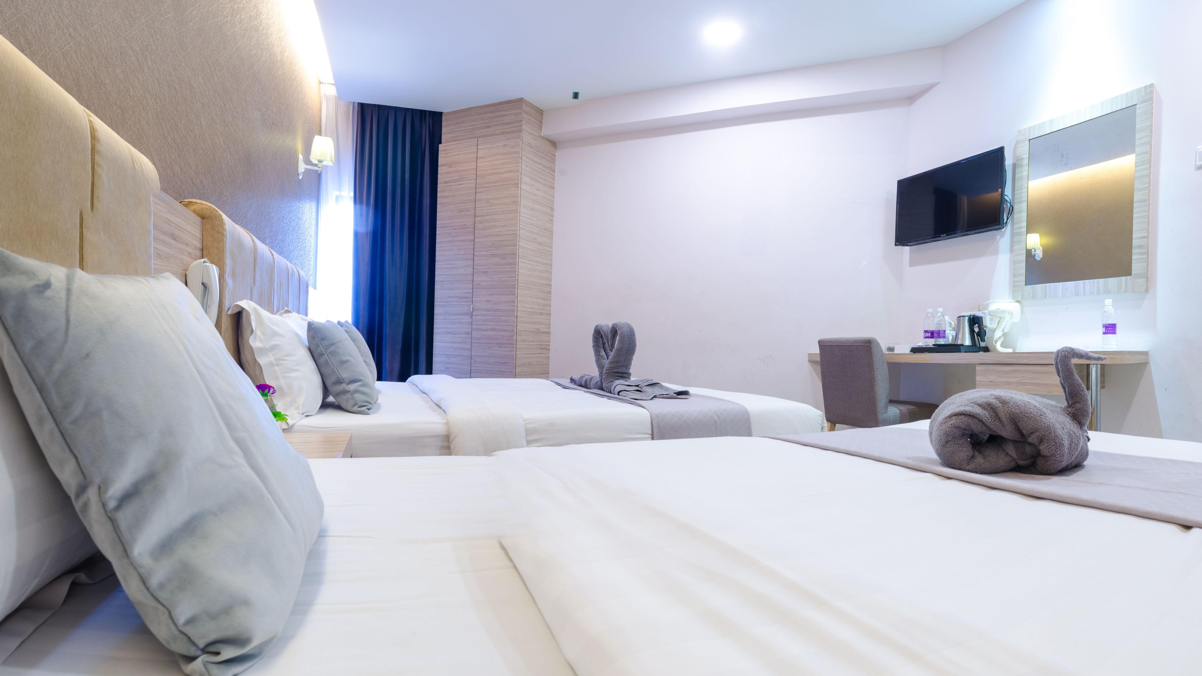 A hotel room with two beds, a desk, a TV, and a bathroom.