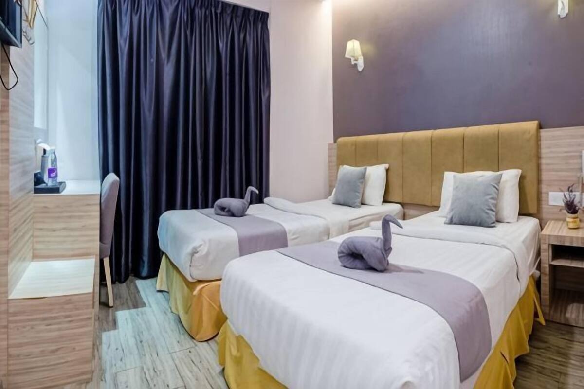 Ein Hotelzimmer mit zwei Betten, einem Schreibtisch, einem Stuhl und einem Fenster mit Vorhängen.