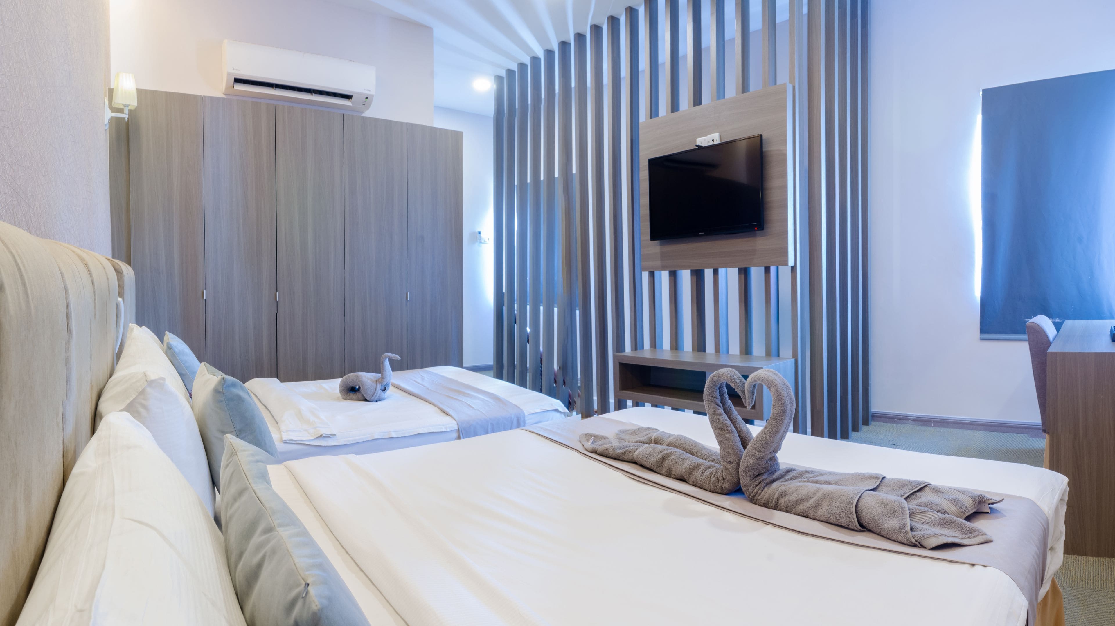 A hotel room with two beds, a flat-screen TV mounted on the wall, and a large window.