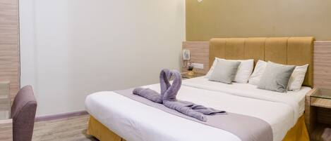 A hotel room with a bed, a nightstand with a phone, a chair, and a wall-mounted lamp.