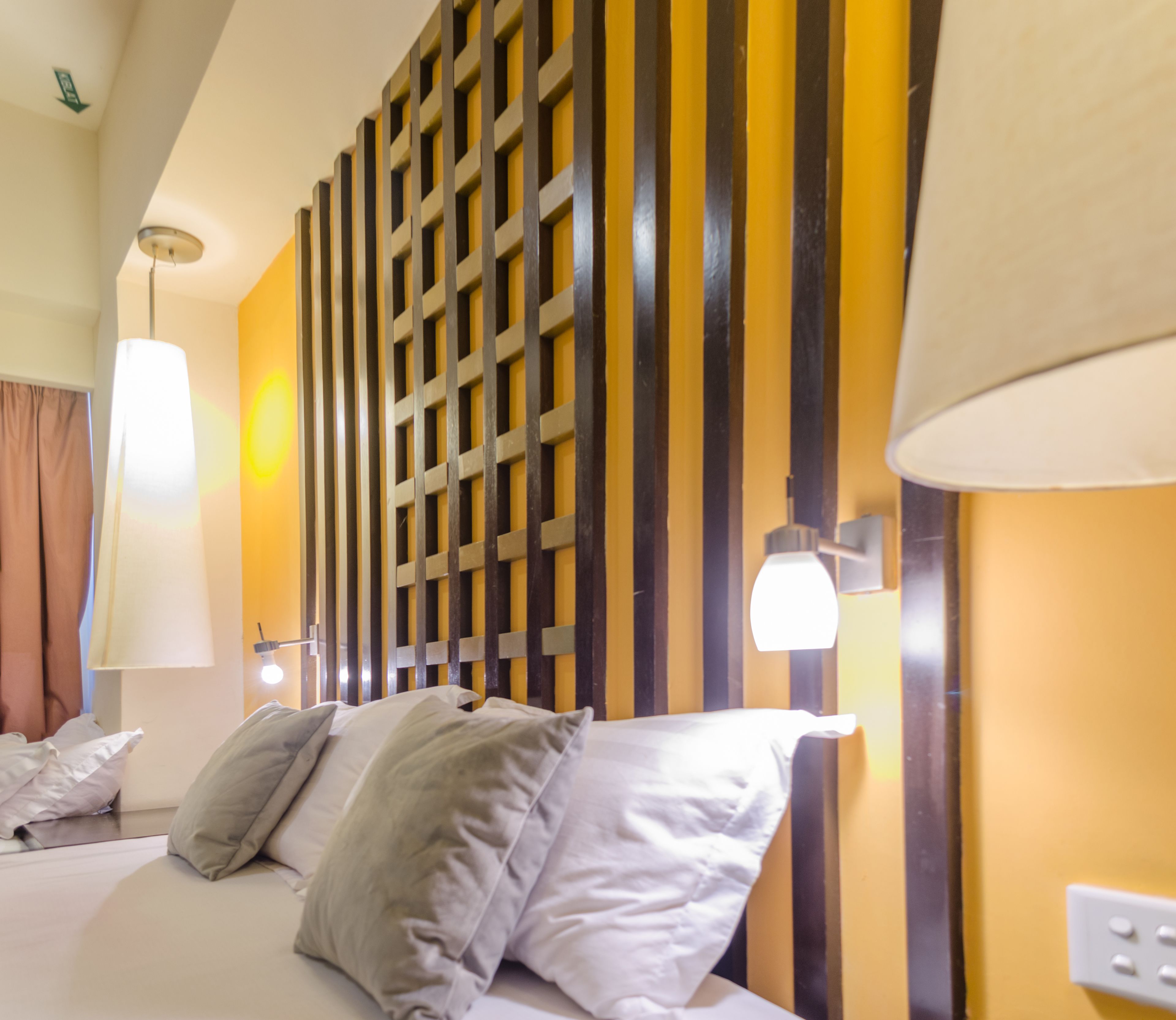 A hotel room with a bed, pillows, a headboard with vertical slats, and two wall-mounted lamps.