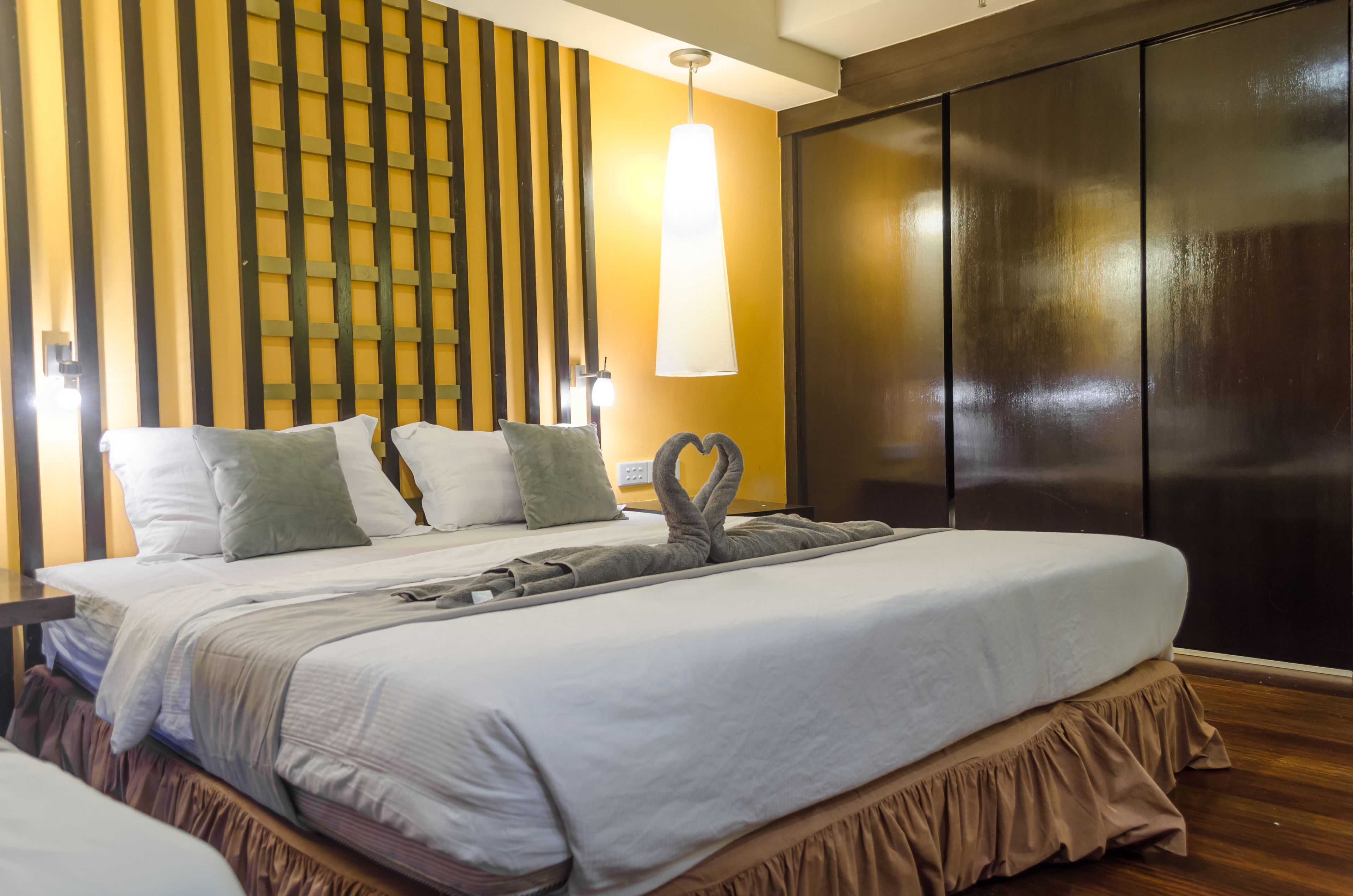 Une chambre d’hôtel avec un grand lit, un mur recouvert de lambris en bois, une armoire sombre et un luminaire suspendu.