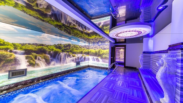Una piscina interior lujosa con un mural de cascada, suelo estampado y una estatua.