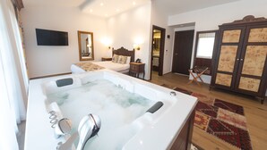 Una habitación amplia con una bañera grande, una cama con cabecero, un armario de madera y un televisor fijado a la pared.