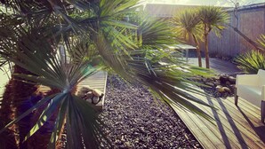 A wooden deck with palm trees, a white bench, and a stone pathway. - Hotel Napoléon (Ile-d'Aix)
